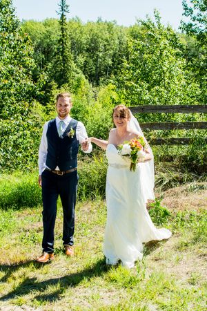 Couple in wedding attire standing together in a lush green outdoor setting.
