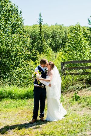 A couple shares an intimate moment outdoors surrounded by lush greenery and a rustic wooden fence.