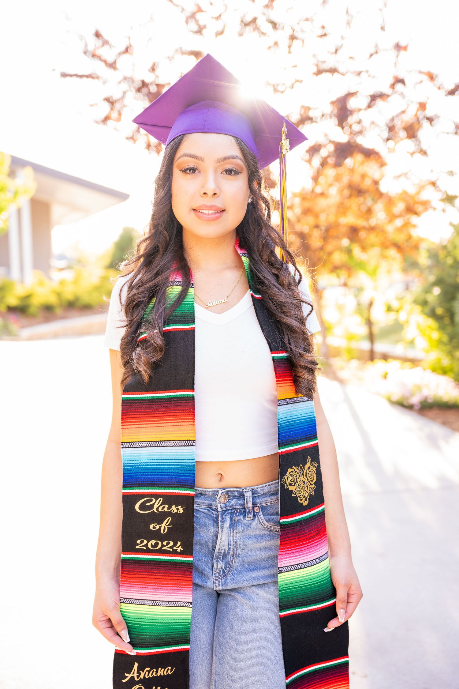 Graduate wearing colorful serape stole and graduation cap poses outdoors.