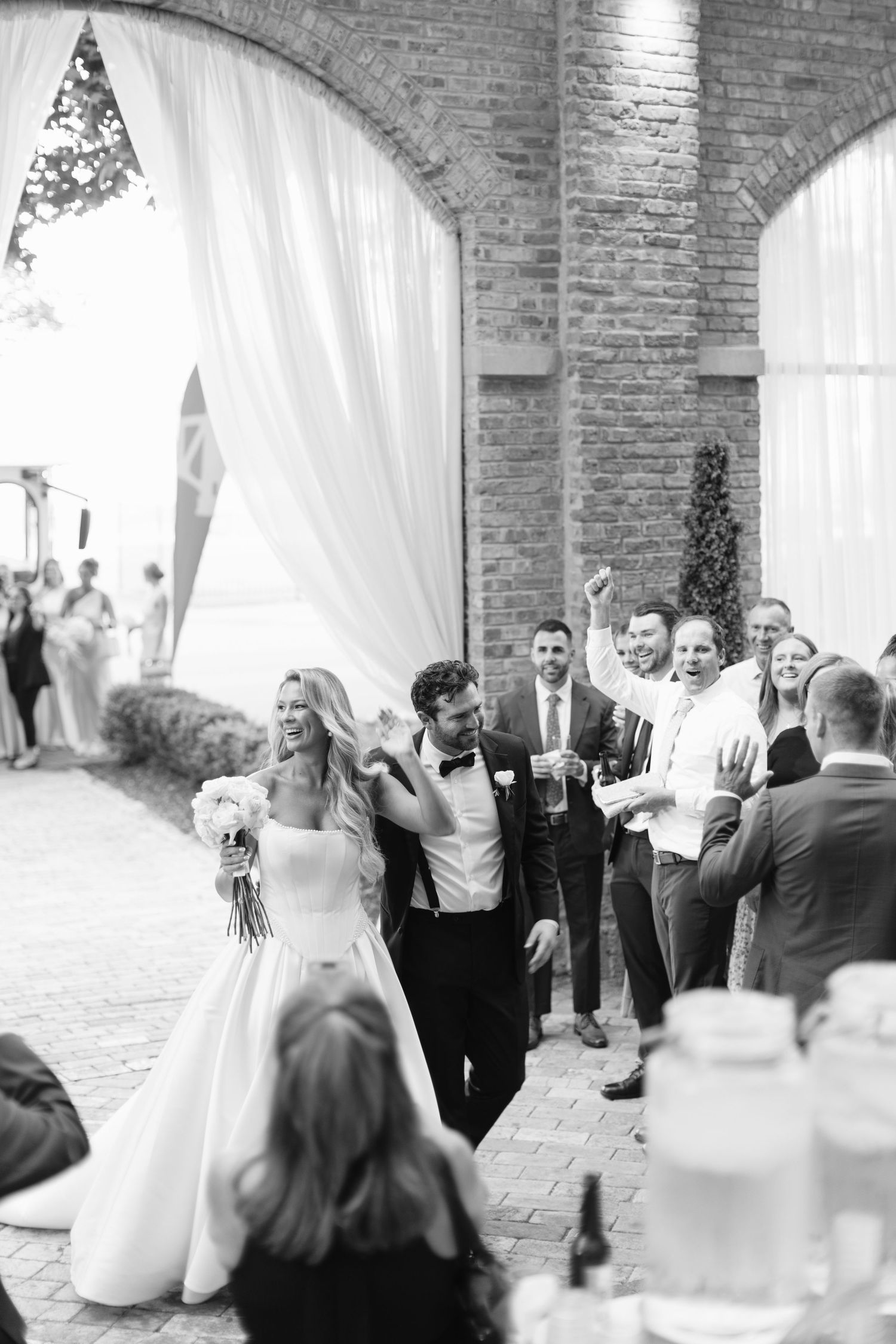 A joyful wedding celebration under brick archways with flowing white curtains as guests gather for the reception.