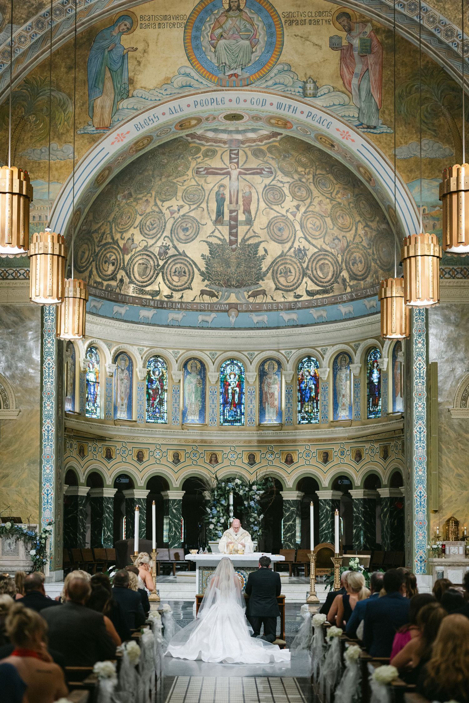Traditional church wedding ceremony with stained glass windows, marble columns and a long flowing white bridal gown.