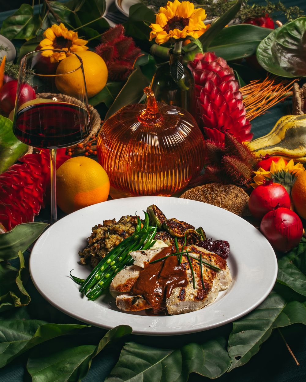 Elegant plated dish with meat and vegetables surrounded by oranges, sunflowers, and wine in a festive setting.