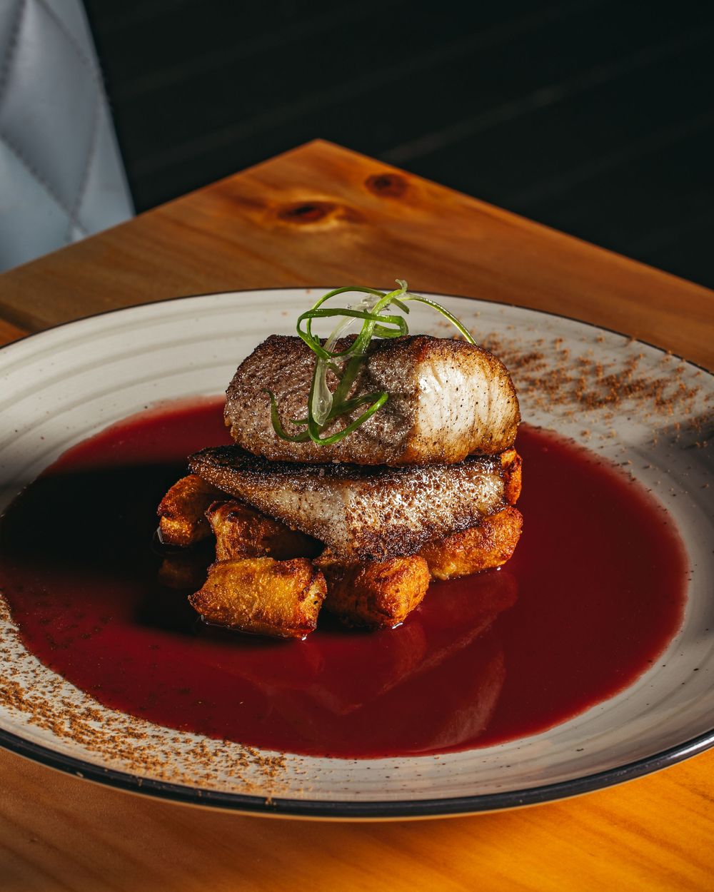 Pan-seared steak served on a vibrant red wine reduction sauce with garnish on a white plate.