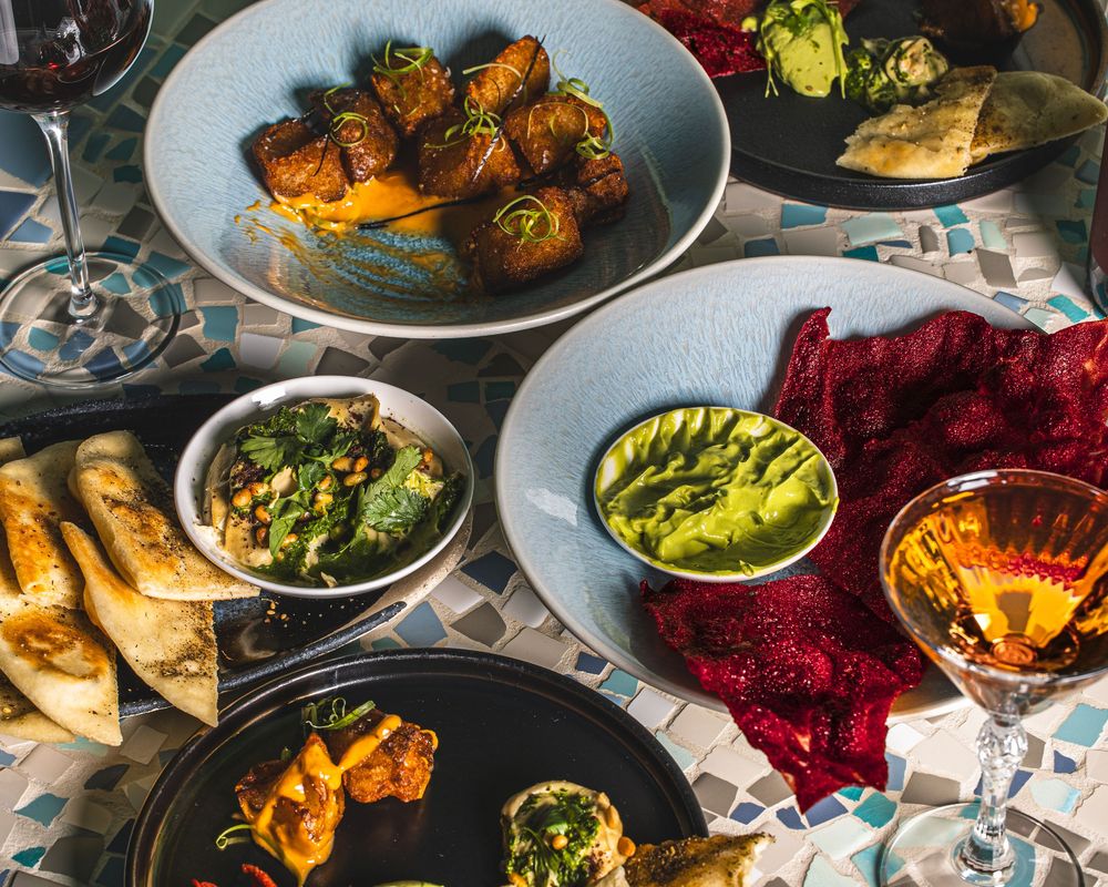 Overhead view of a restaurant table with multiple colorful dishes including roasted vegetables and vibrant side dishes.