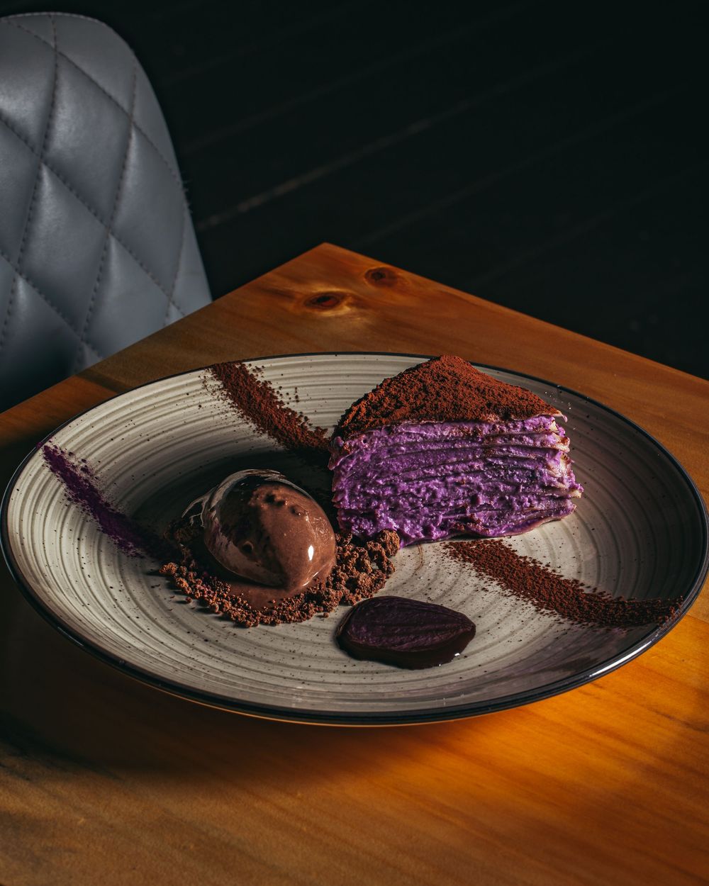 A sequence of chocolate desserts with purple accents on a gray ceramic plate against a dark background.