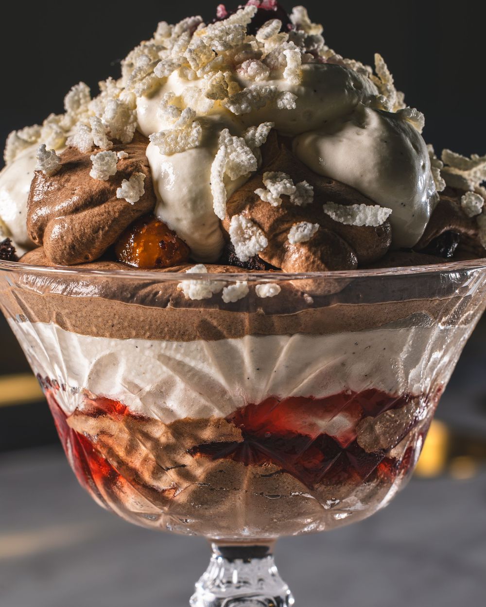 A decadent chocolate dessert layered with cream and berries served in an elegant glass footed dish.