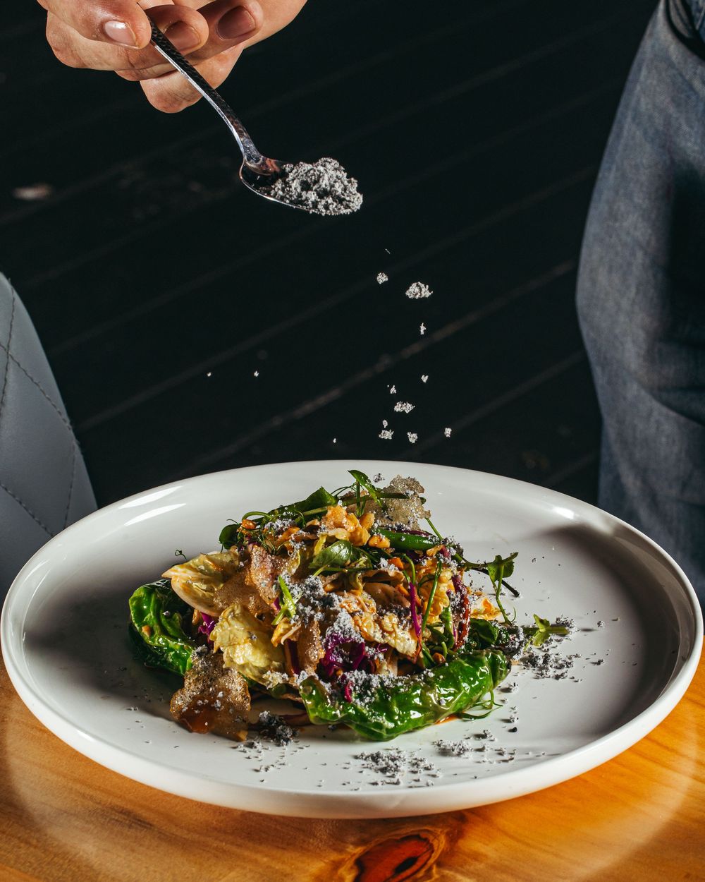 Chef garnishing a plated dish with microgreens and finishing touches in a fine dining restaurant setting.