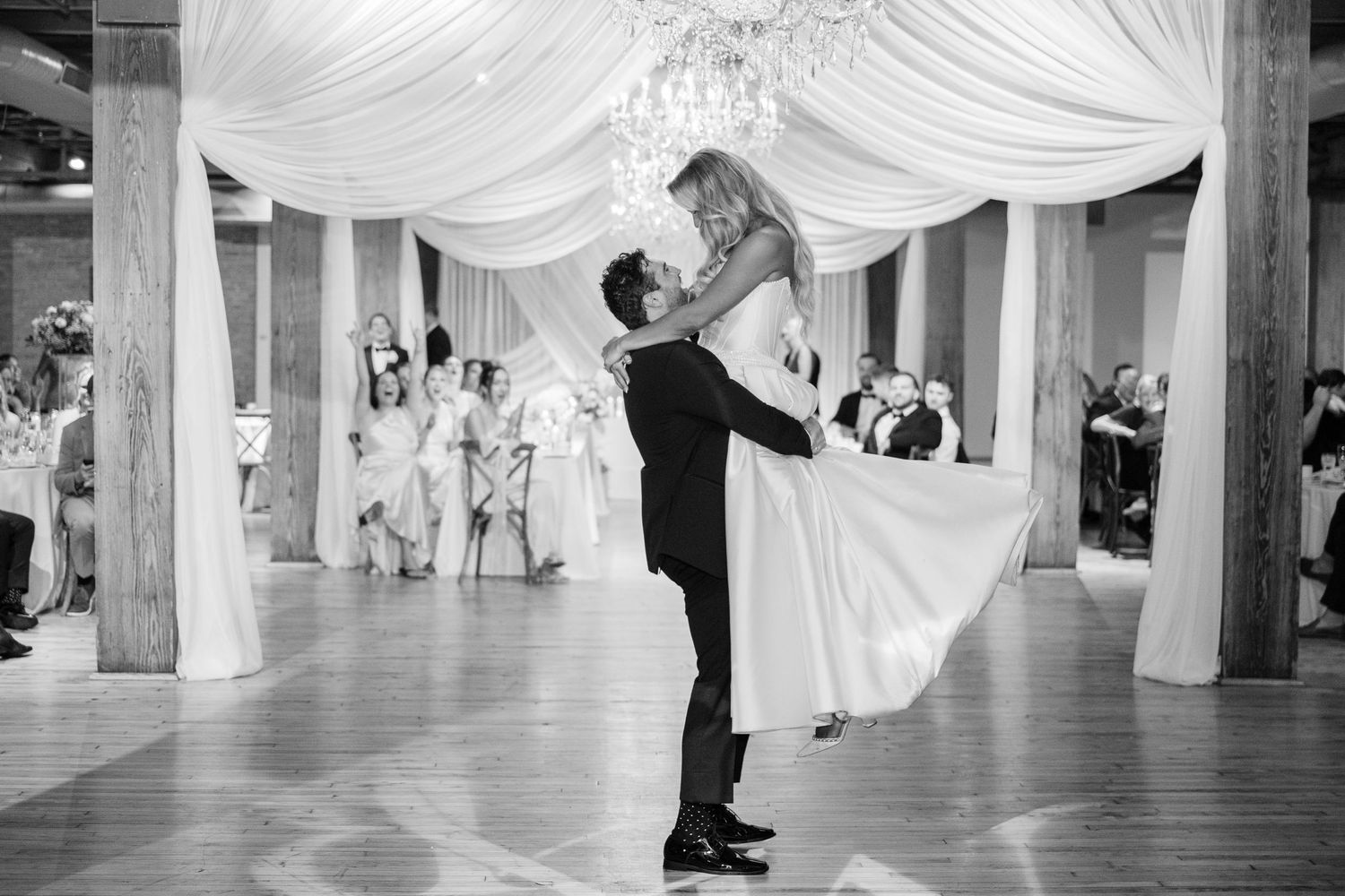 A black and white wedding dance sequence showing a dramatic dip on a draped ballroom floor.