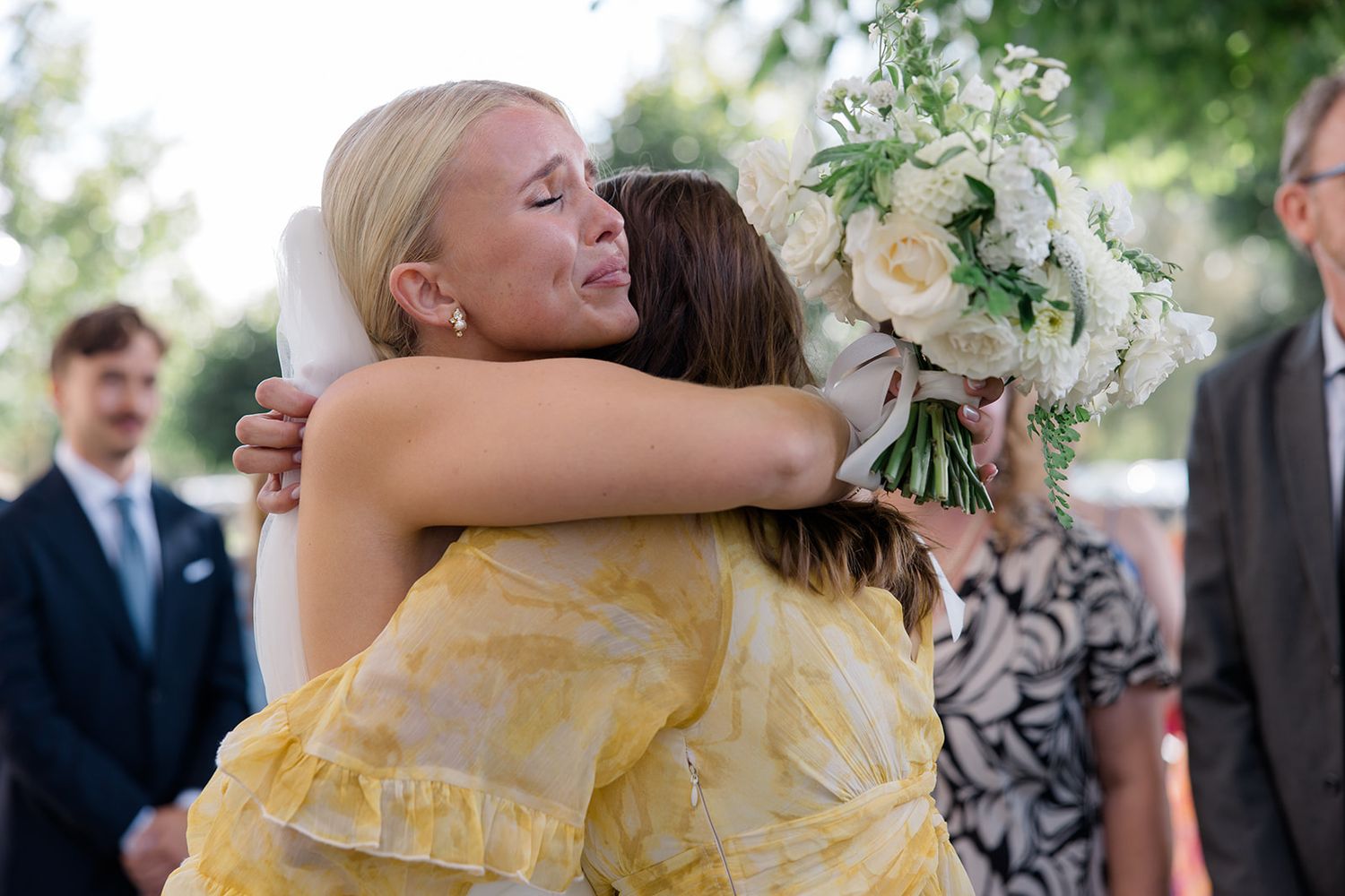A couple embraces and dances together at an outdoor wedding reception surrounded by guests and greenery.