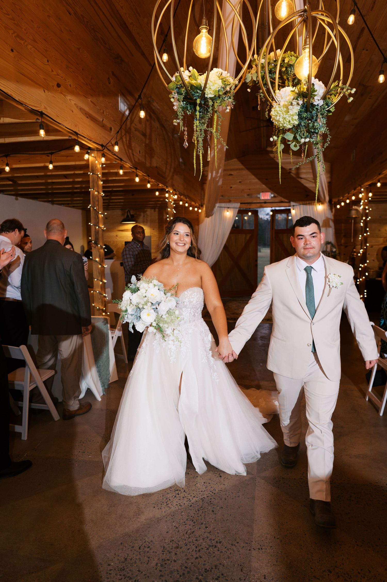 A wedding celebration in a rustic barn venue decorated with string lights and floral chandeliers.