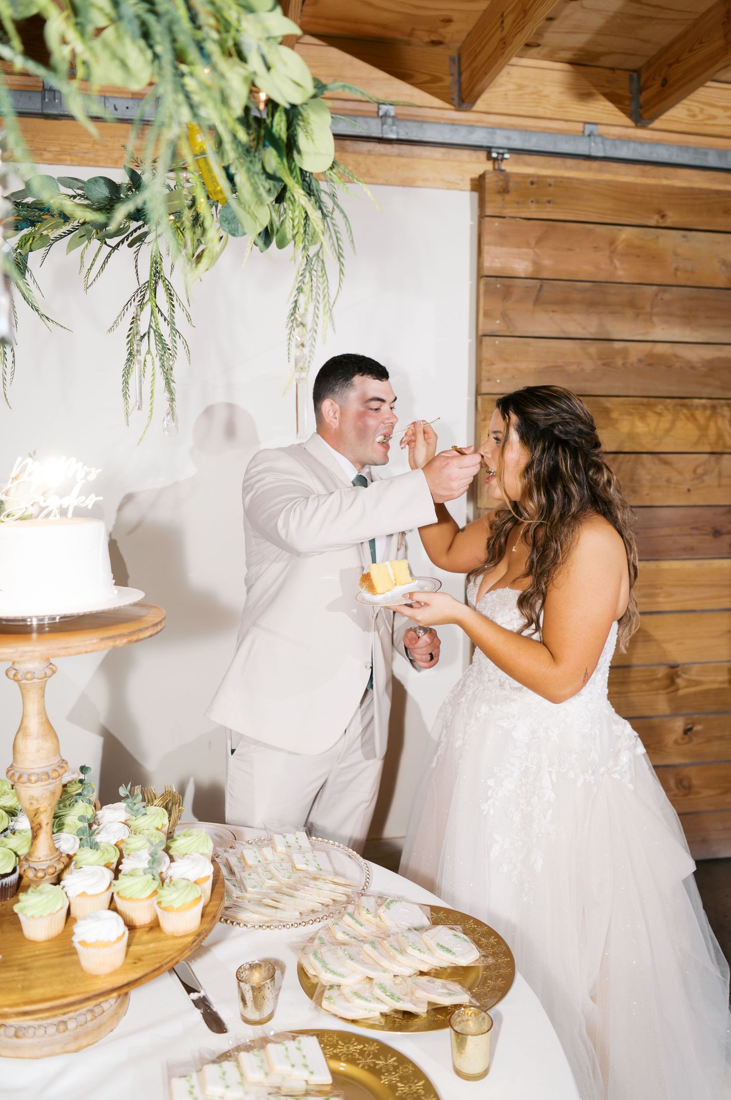 Newlyweds share a playful moment while cutting their wedding cake at a rustic wooden venue.