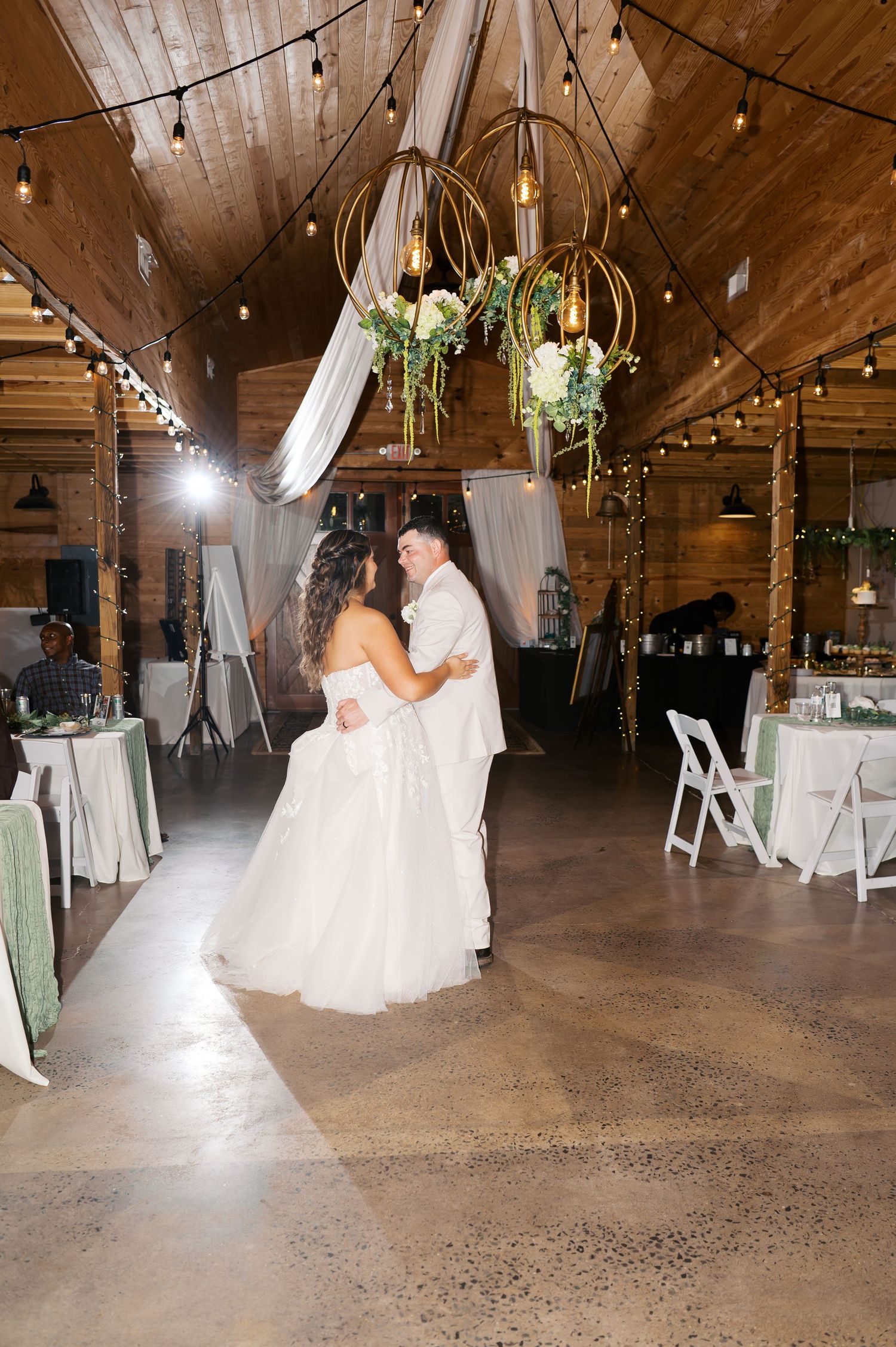 Elegant wedding venue with wooden beams, string lights, and white drapes creating a romantic rustic atmosphere.