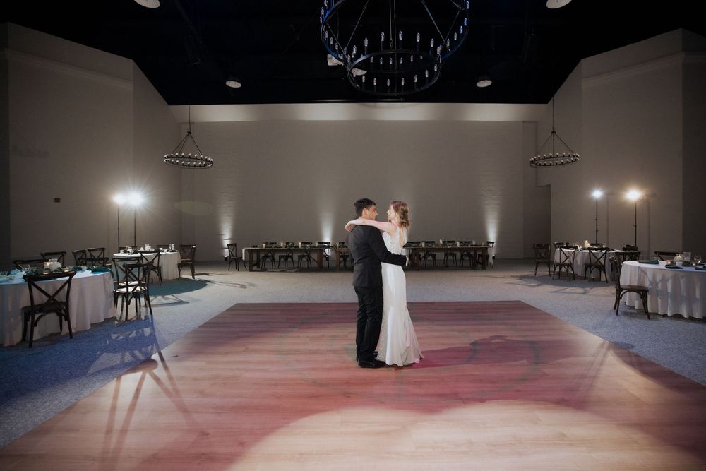 A couple shares their first dance on a pink-lit dance floor in a spacious reception hall during their wedding celebration.