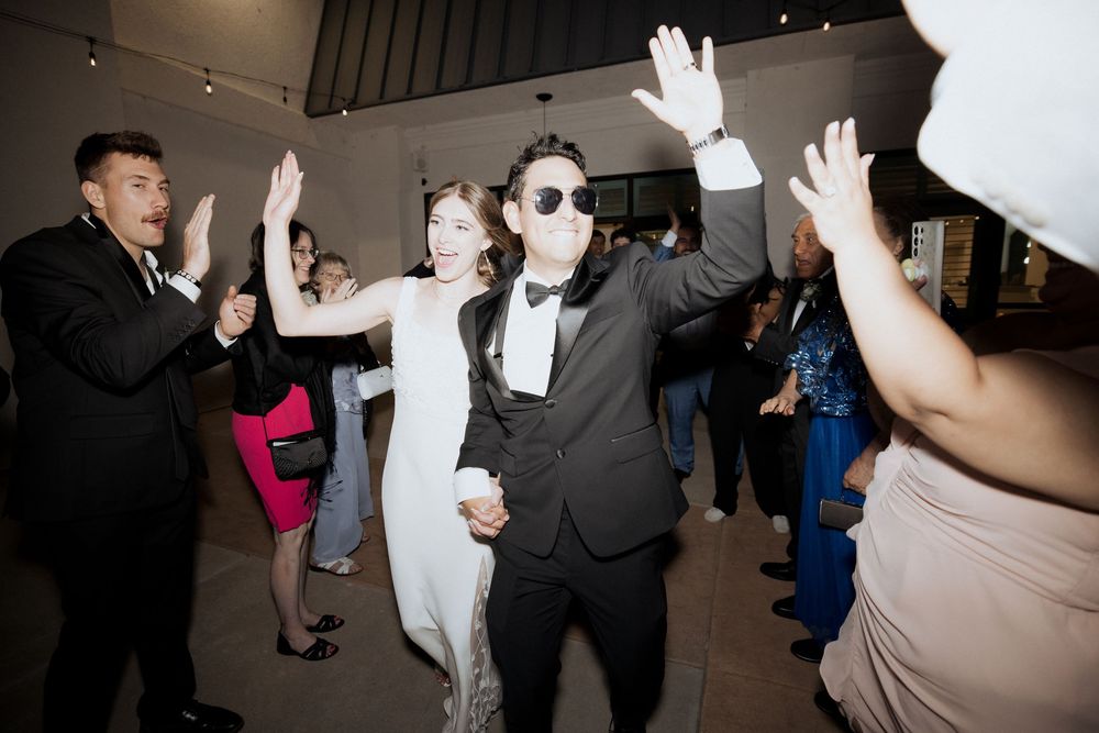 Wedding guests dance and celebrate on a dark dance floor at a reception party.
