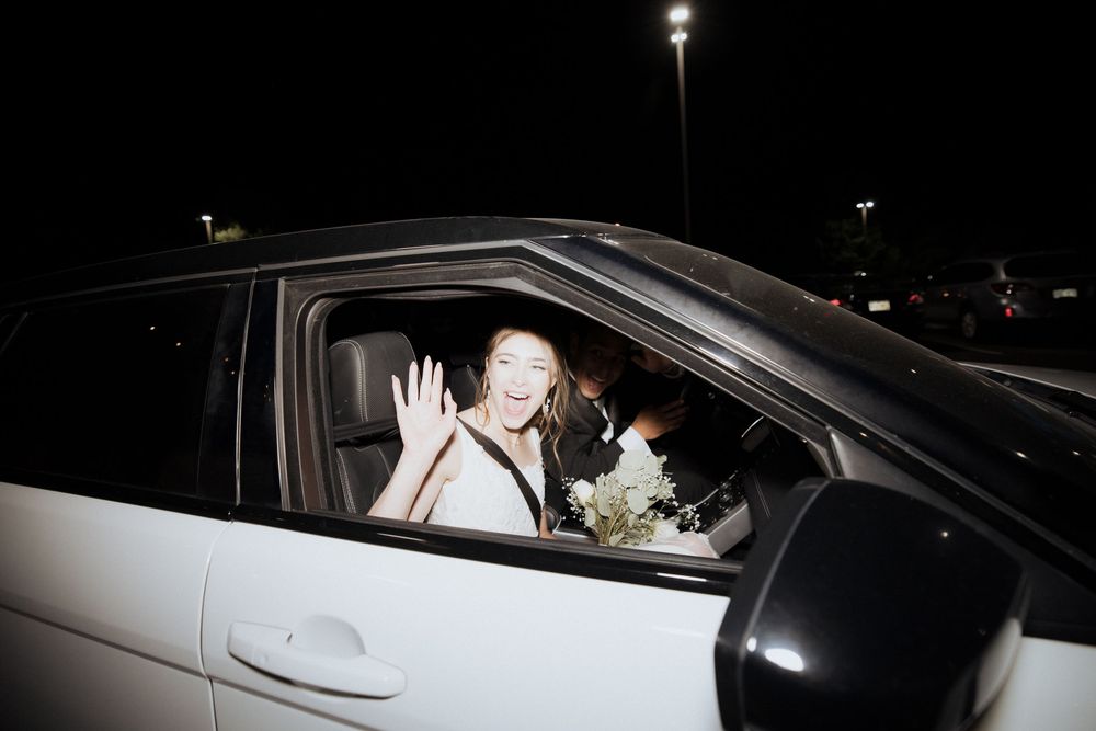 Paparazzi photograph of a person in a black car at night through a car window.