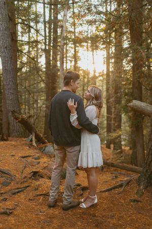 A romantic sunset engagement photo of a couple embracing in a pine forest.