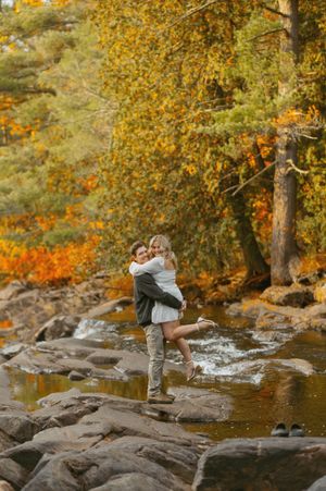 A couple sharing a joyful moment on rocky terrain with autumn foliage in the background.