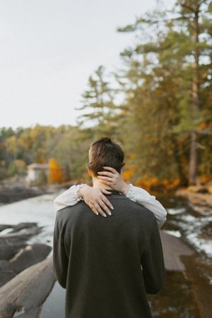 An intimate embrace captured from behind with autumn scenery and flowing water in background.