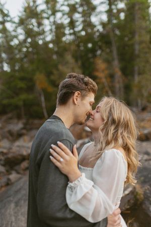 A tender moment between a couple against a backdrop of evergreen trees and autumn colors.