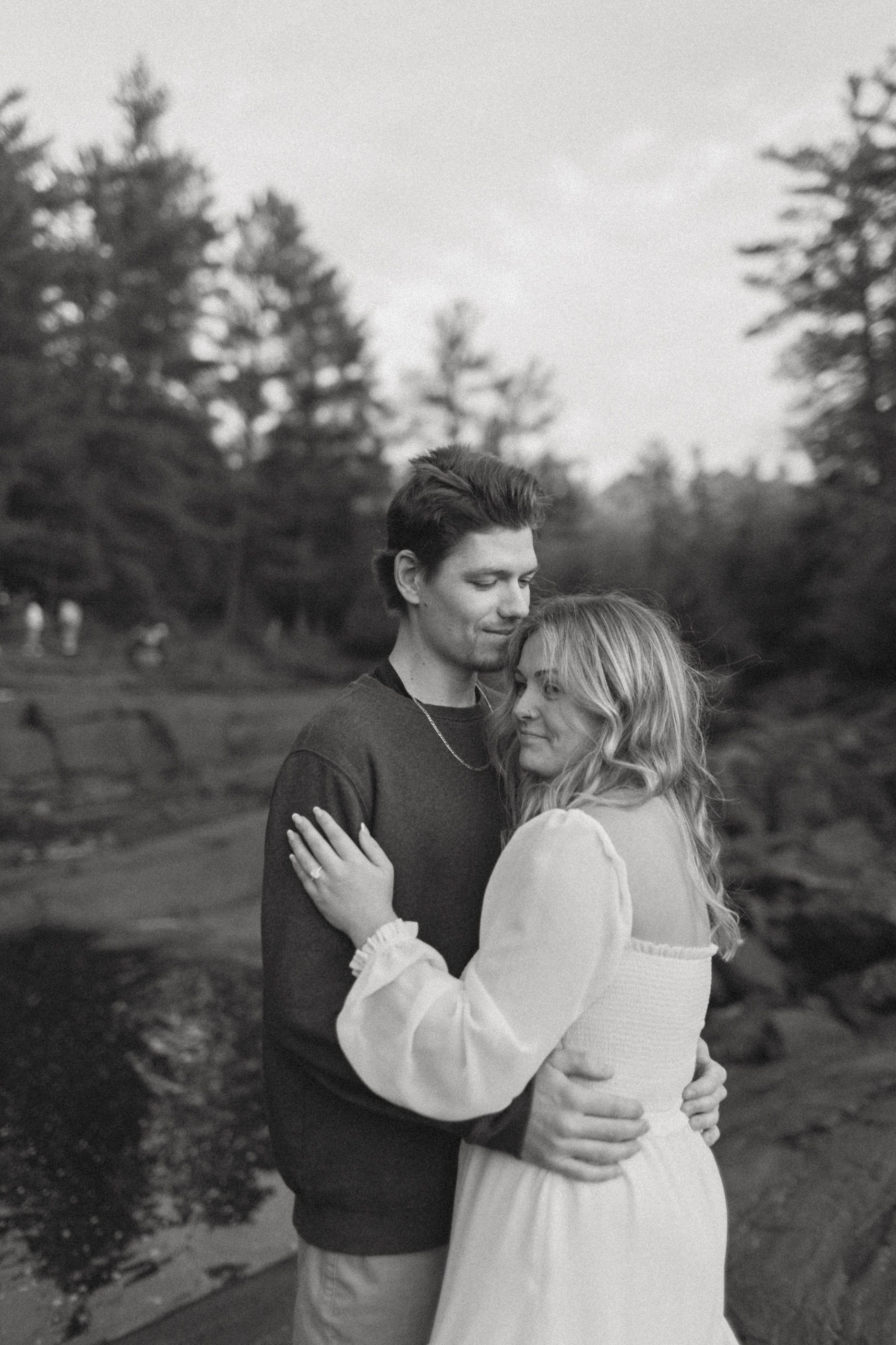 A black and white portrait of a couple sharing an intimate embrace outdoors.