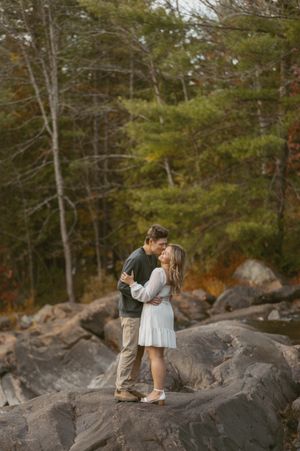 A romantic engagement photoshoot on rocky terrain surrounded by autumn trees and evergreens.