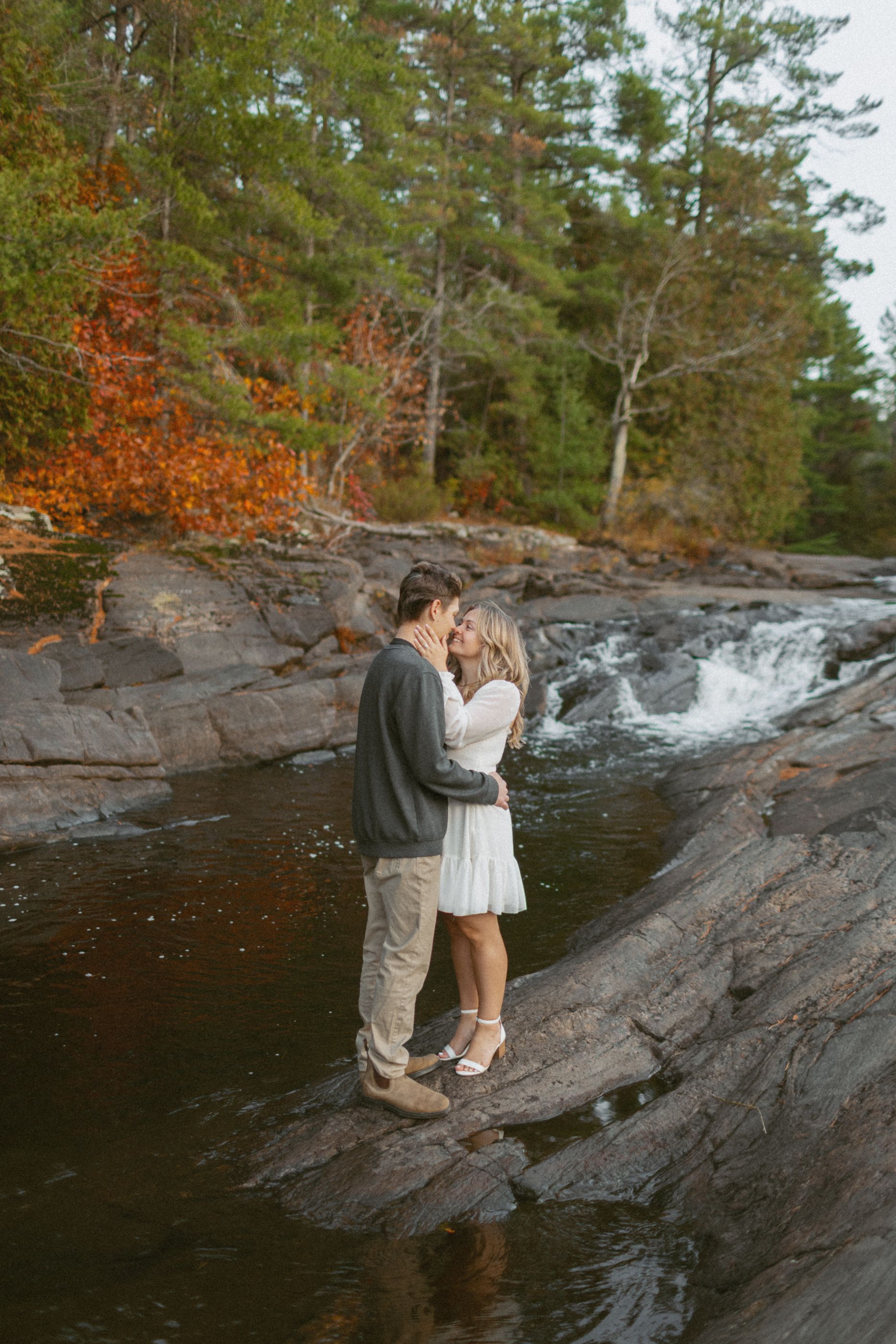 Couple sharing an intimate moment on rocky cliffs beside a flowing waterfall.