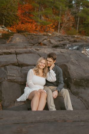 Couple sitting together on dark rocky outcrop during autumn sunset.