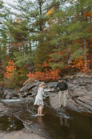 Couple exploring rocky waterfall area surrounded by vibrant fall foliage.