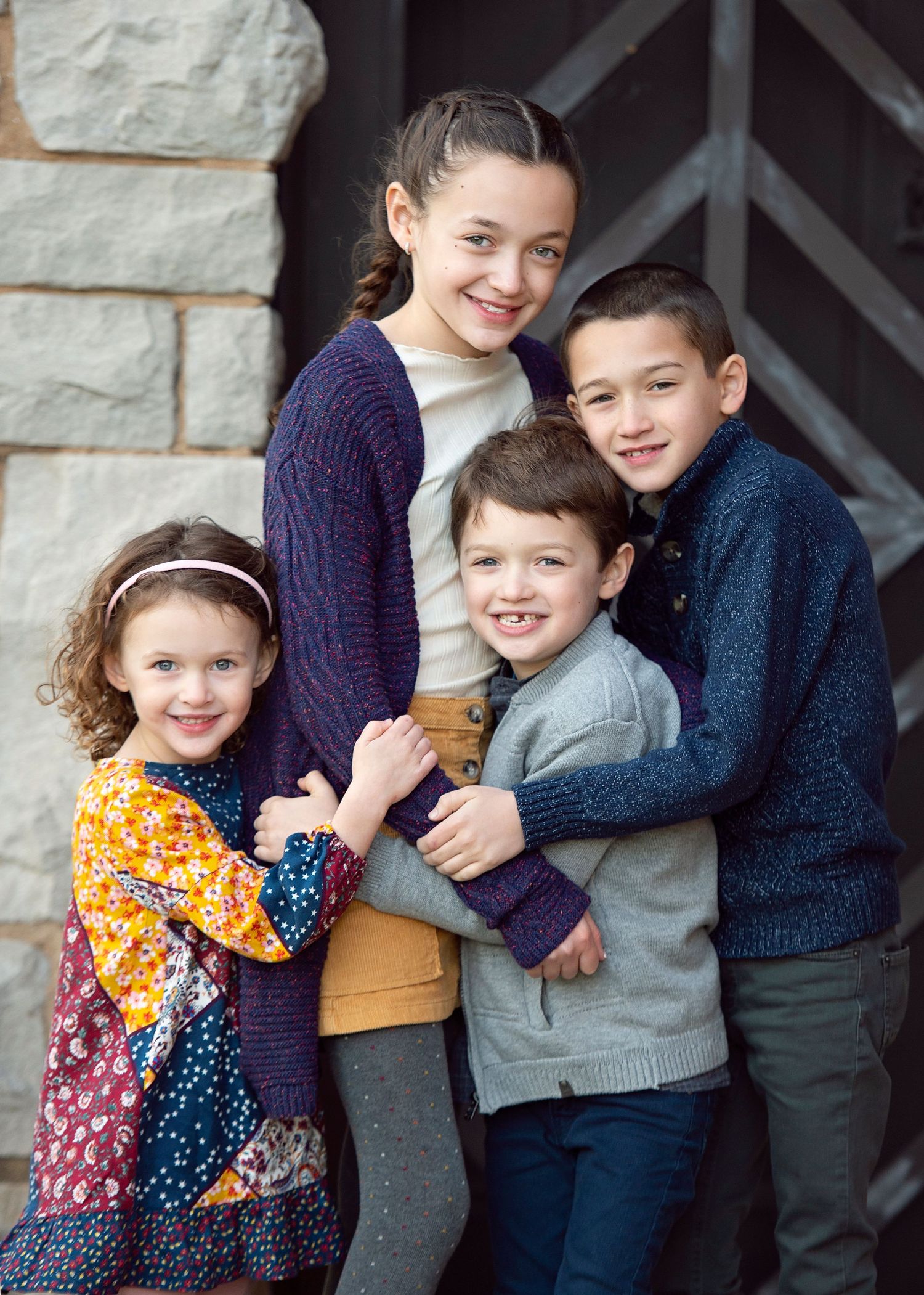 Four happy children posing together for a family portrait outdoors, smiling warmly in casual and colorful outfits.