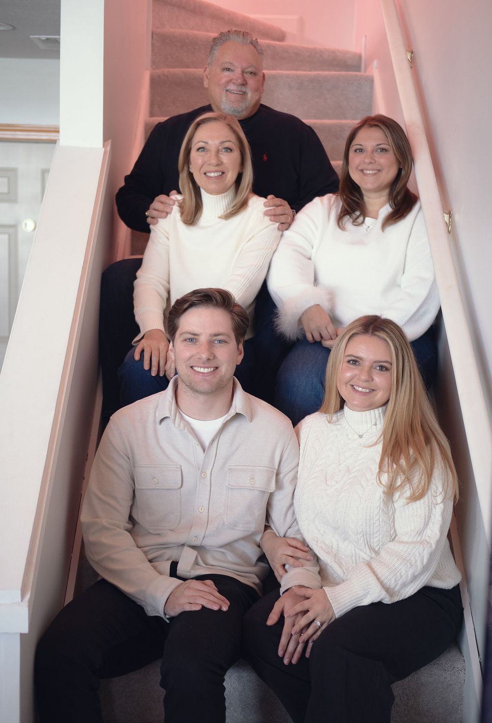 A group of five people wearing white sweaters pose together on wooden stairs in a casual family portrait.