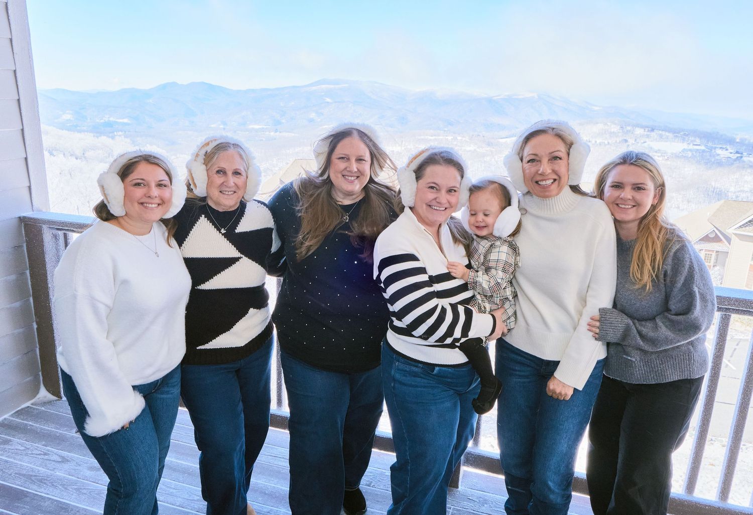 A group of people stand together in a line against a snowy mountain backdrop on a winter day.