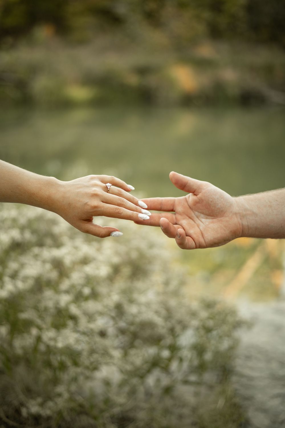 Two hands reaching towards each other against a blurred natural background with white flowers.