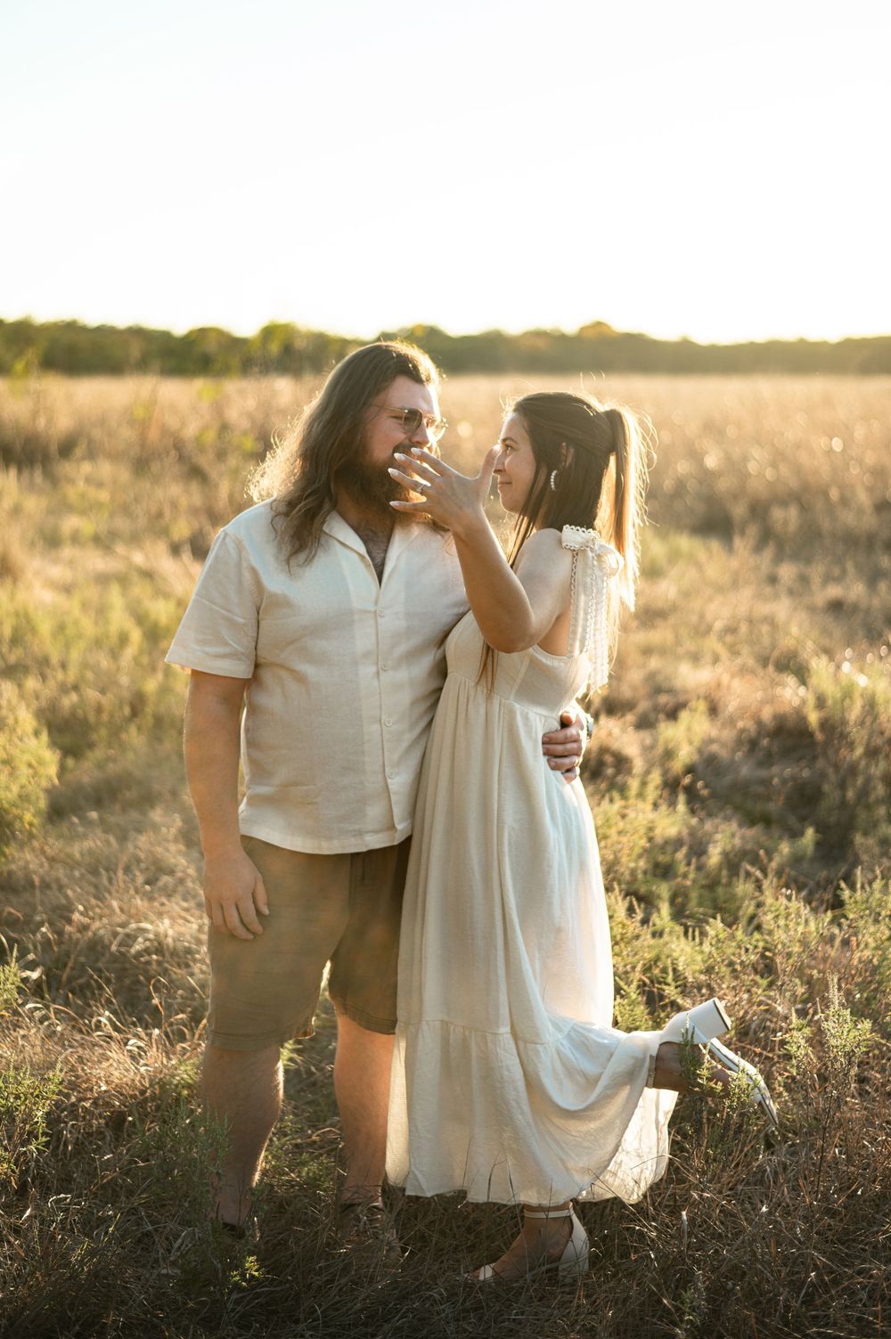 A couple embraces in a sunlit field during golden hour, sharing an intimate moment against a natural backdrop.