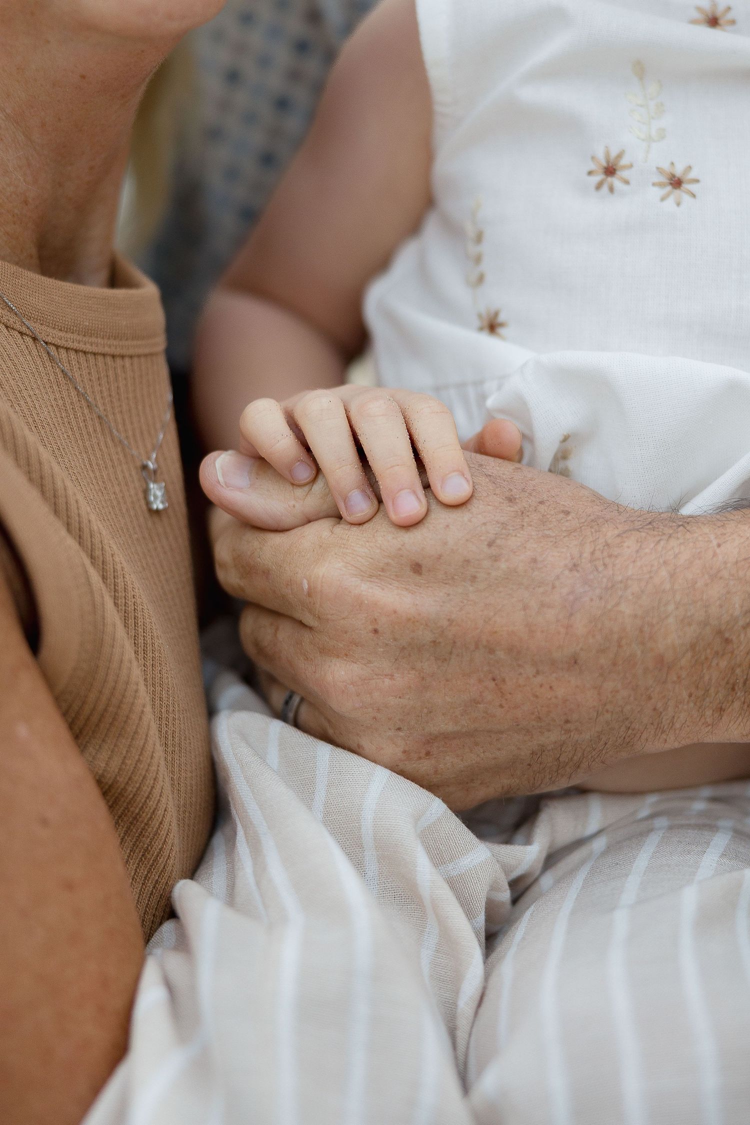A small child's hand gently holds an elderly person's wrinkled hand against white fabric with embroidered stars.