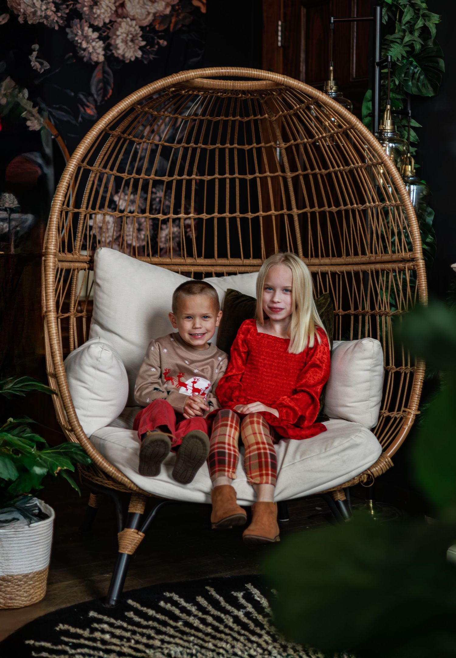 A child wearing a tan holiday sweater with reindeer and snowflake designs sits smiling on a couch.