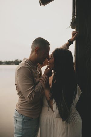 Romantic couple sharing an intimate moment at sunset by the water in muted tones.