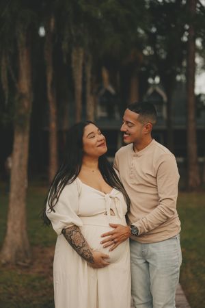Couple in matching light-colored outfits sharing tender moments in a wooded outdoor setting.