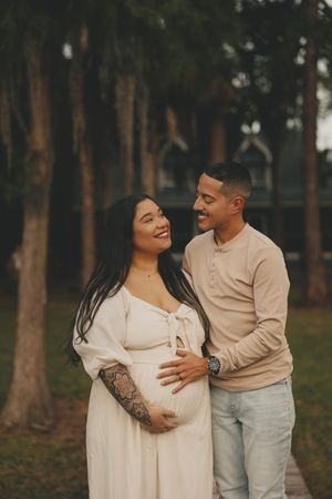 An expecting couple shares tender moments among tall trees during an outdoor maternity photoshoot.