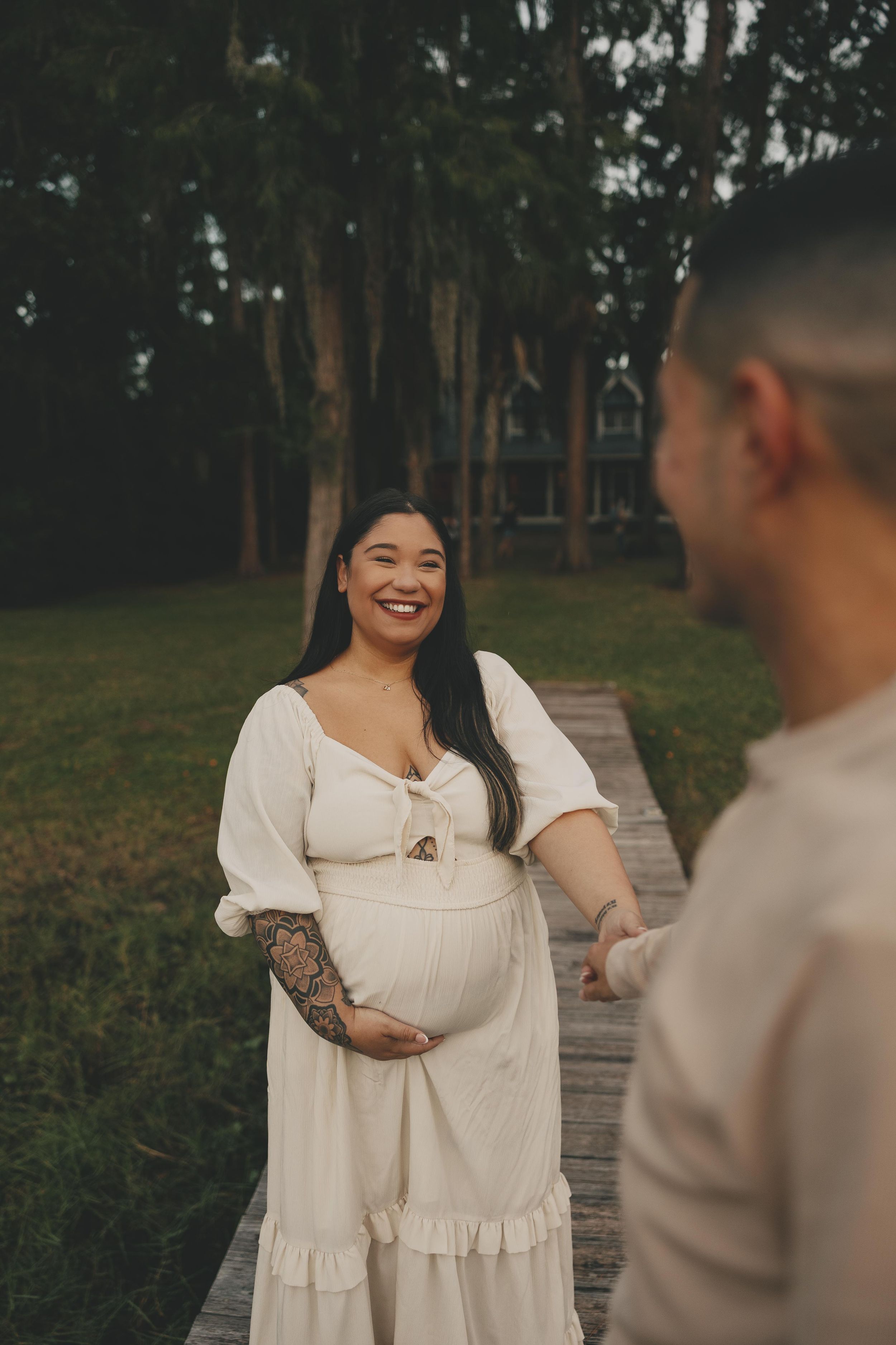 A couple in white outfits shares romantic moments outdoors in a natural setting with trees.