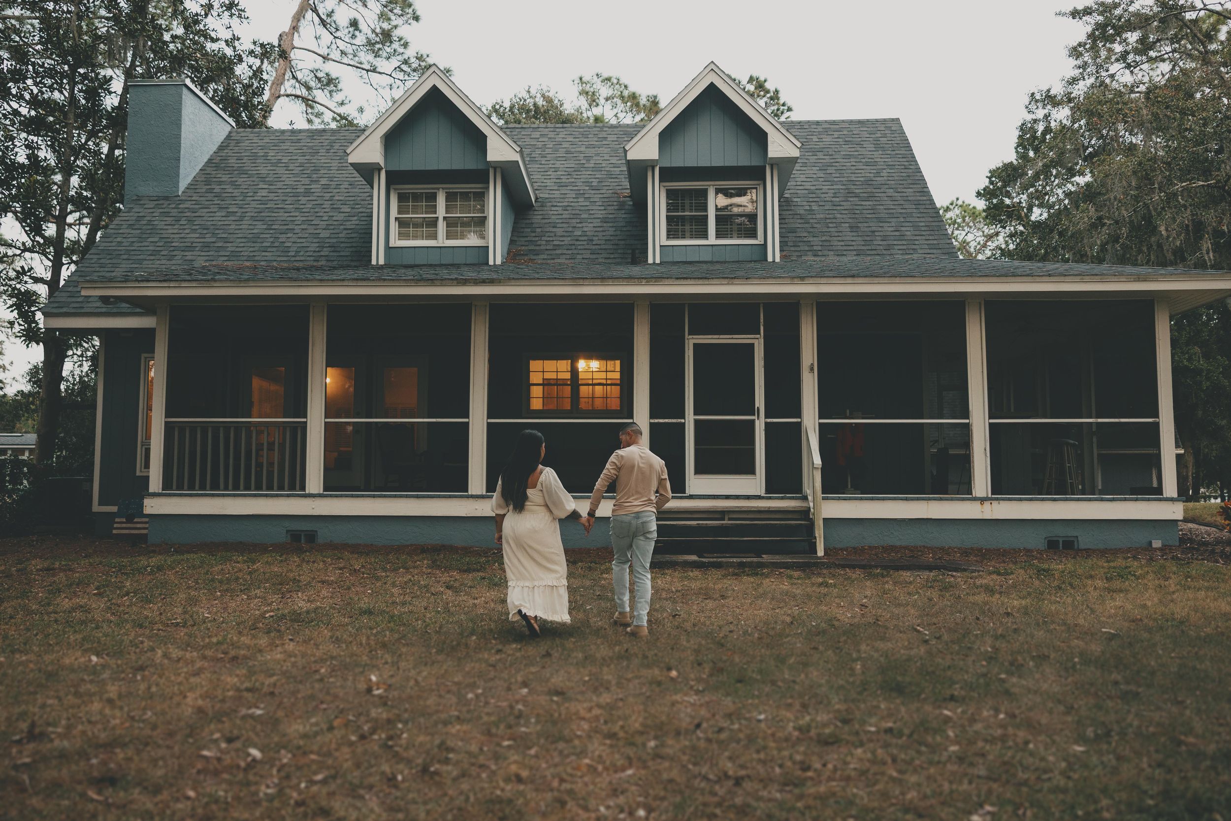 A rustic farmhouse with wrap-around porch and dormers is shown in a series of exterior views at dusk.
