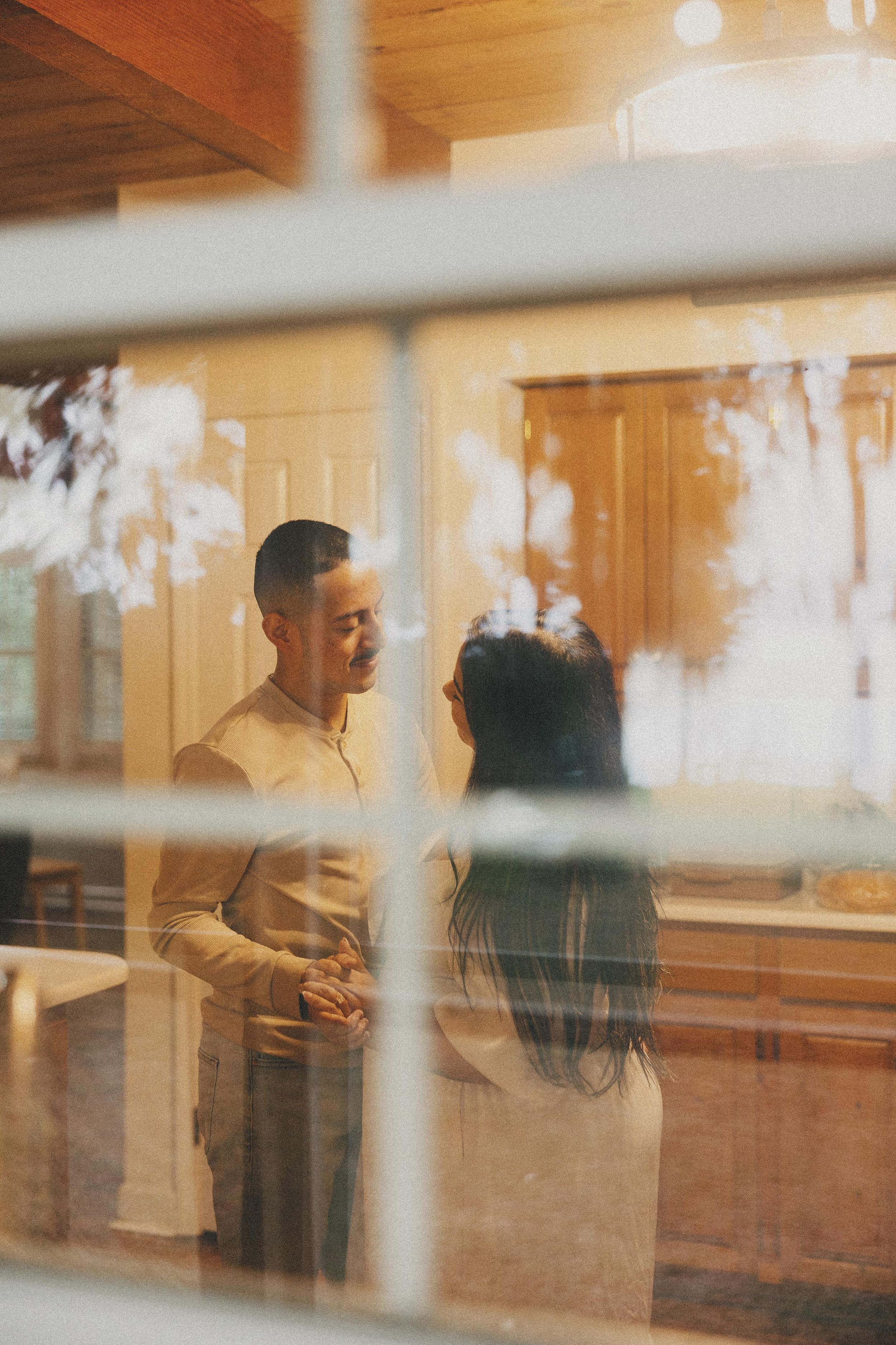 Romantic couple embracing through window reflections in a sunlit room.