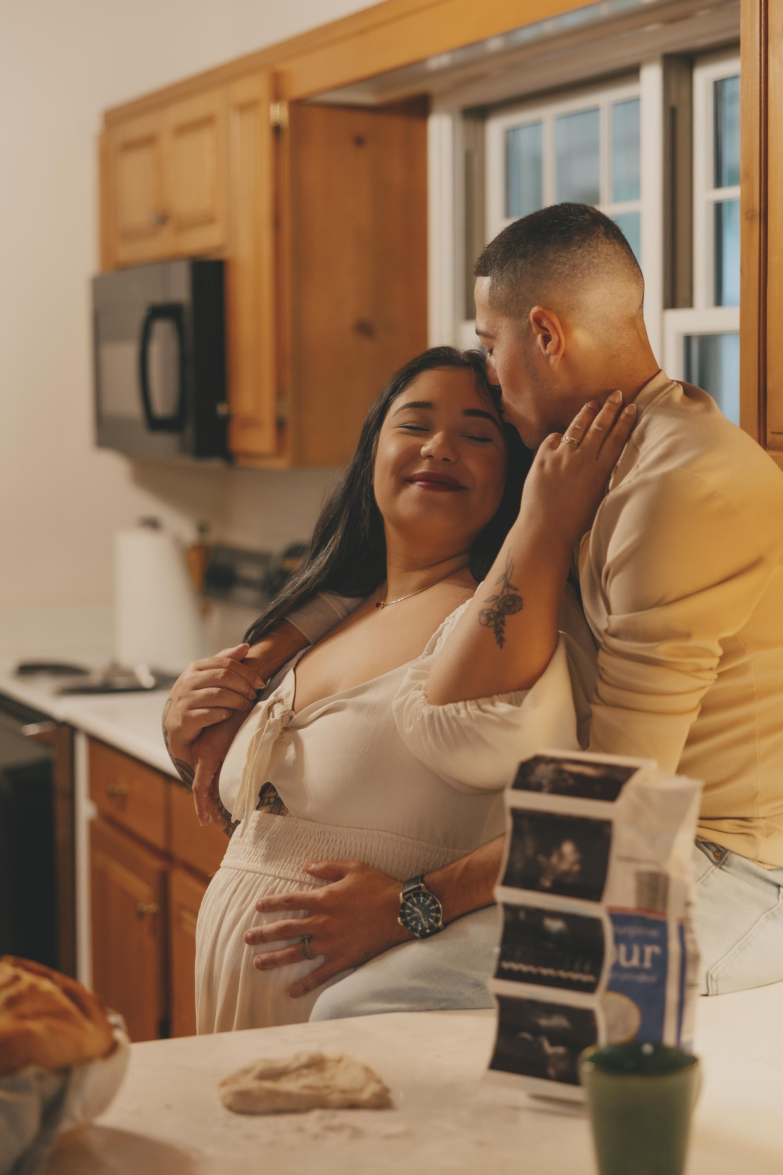 Couple shares tender moments in their kitchen while looking at ultrasound photos together.