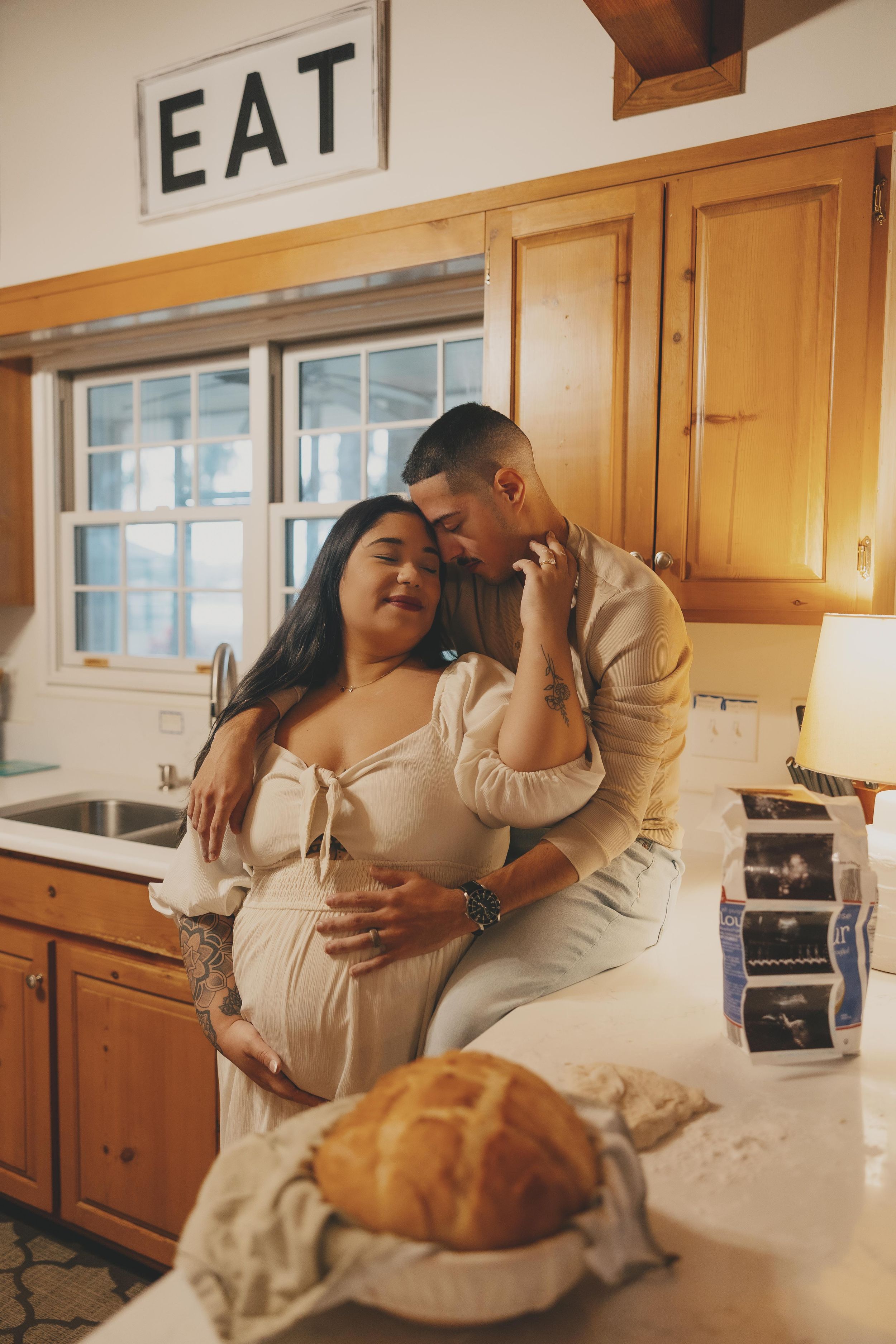 Couple sharing intimate moments in a cozy kitchen with wooden cabinets and warm lighting.