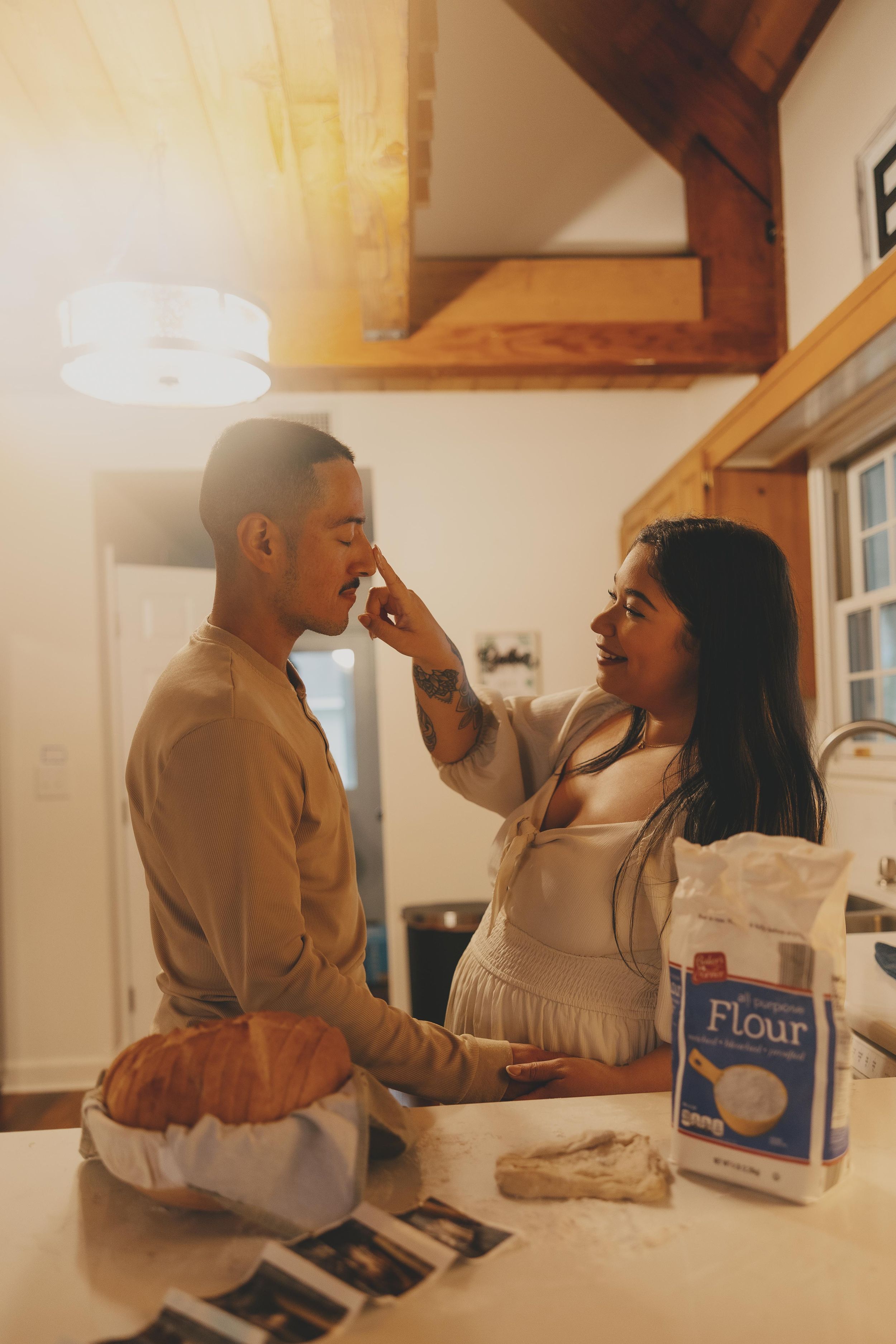A couple playfully shares intimate moments while baking together in a warmly lit kitchen.