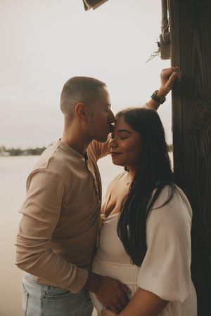 A couple embraces tenderly against a white wall during a romantic photoshoot.