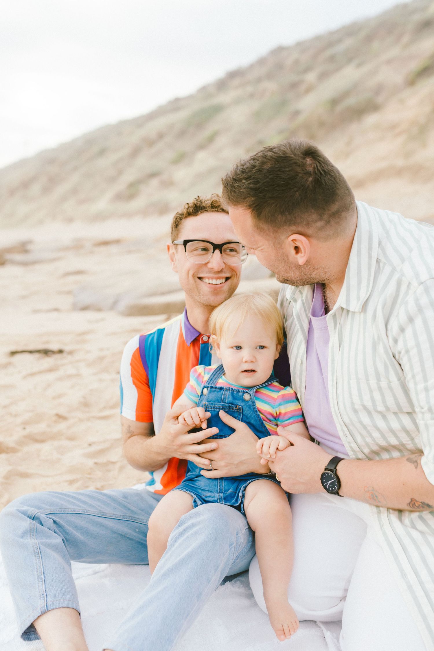 Family enjoying tender moments together on a sandy beach during a photo session.
