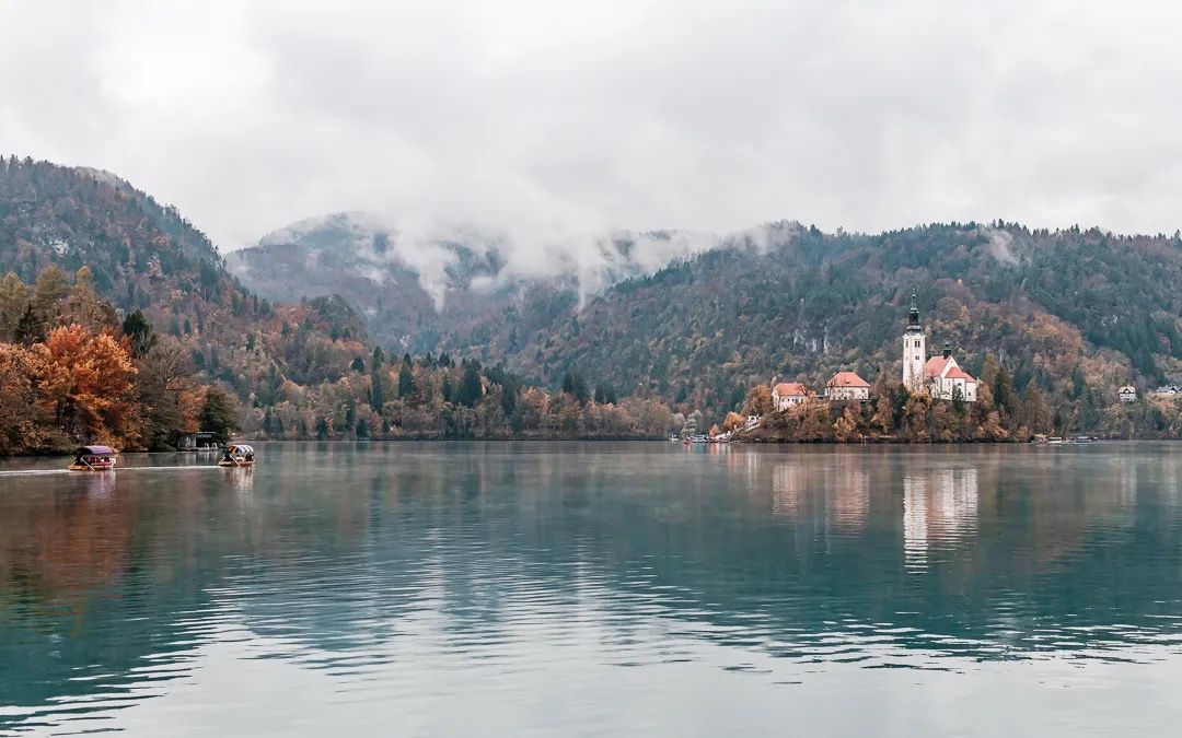 Lake Bled landscape with church island, soft mist, and mountain reflections on the water.