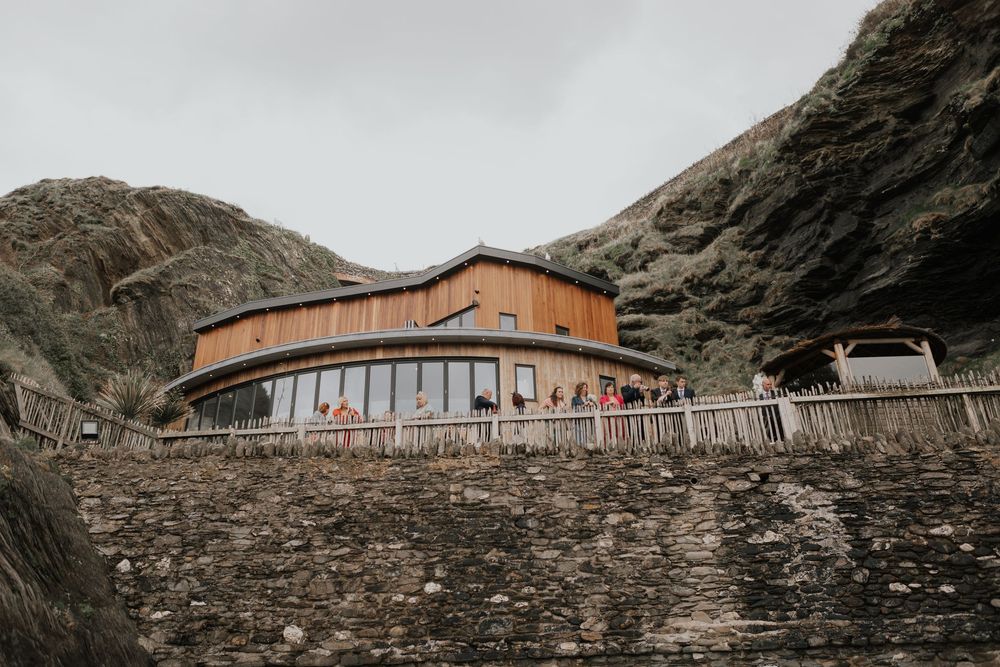 Modern curved wooden wedding venue nestled between dramatic rocky cliffs by the coast.