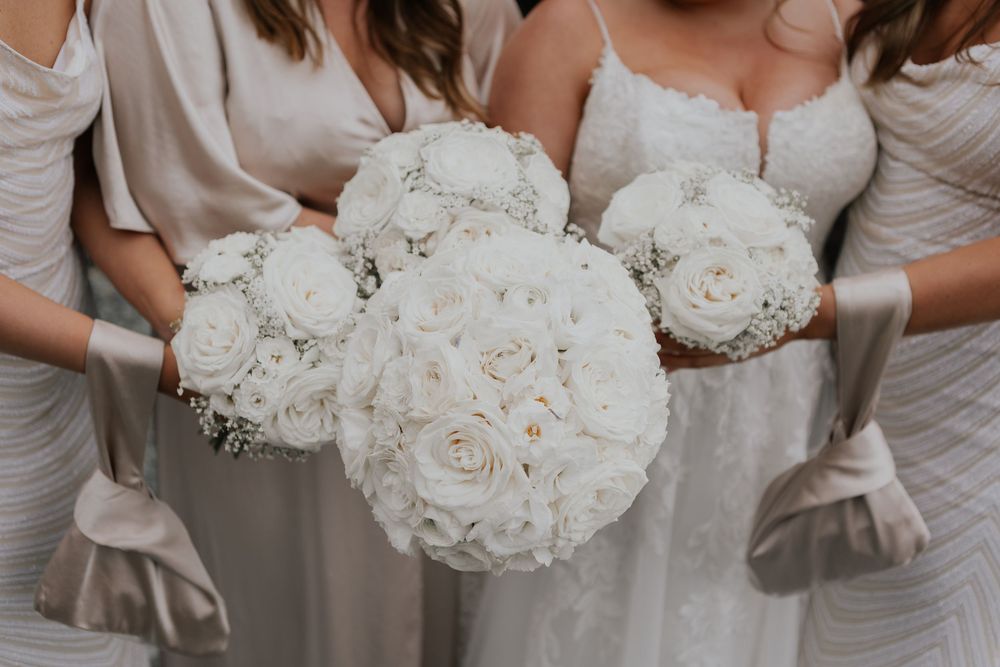 Close-up of white rose bridal and bridesmaid bouquets held by wedding party in champagne dresses.