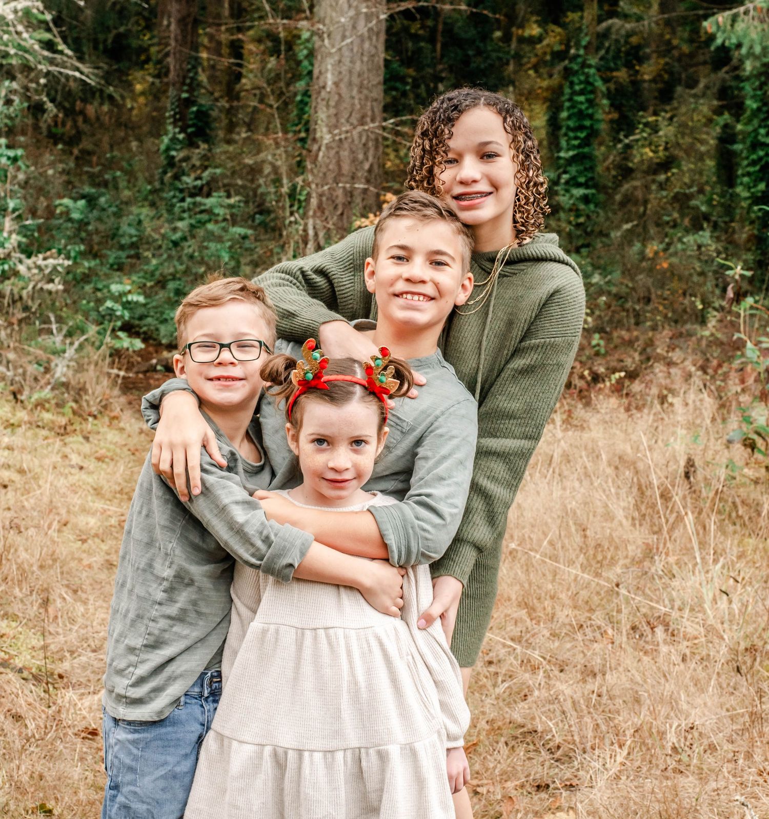 Three siblings share warm embraces while posing together in a wooded outdoor setting during golden hour.